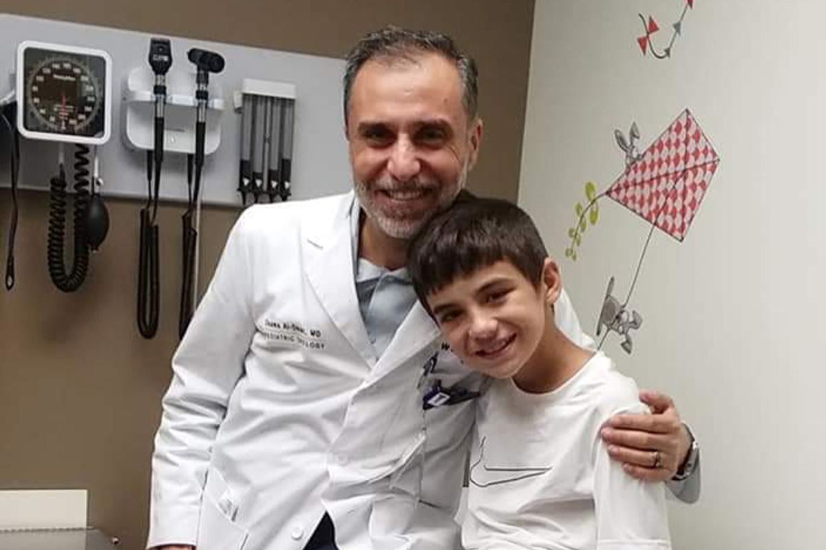 a medical professional sits with his arm around a pediatric patient