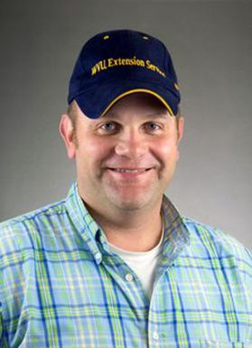 A man wearing a blue and gold WVU Extension hat with a light blue flannel.