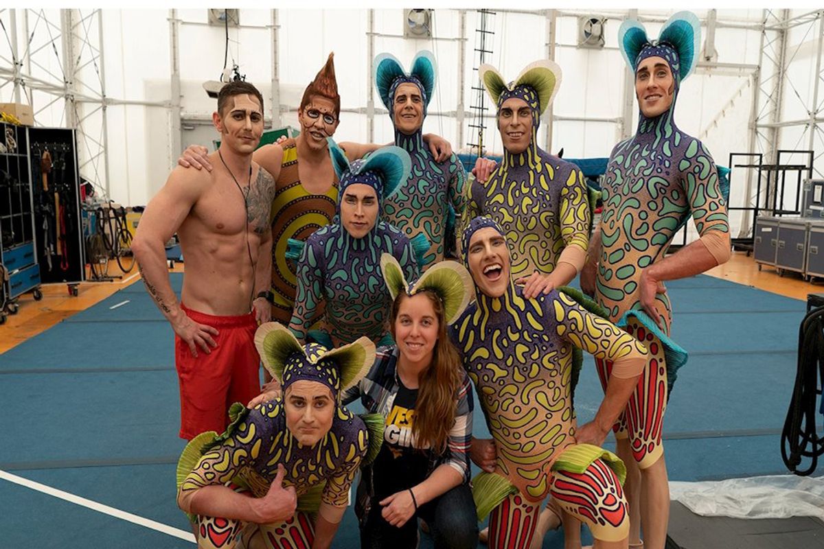Nine members of a Cirque de Soleil cast pose for a picture together for a picture dressed in their brightly colored costumes.