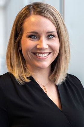 Headshot of WVU Executive Director of Student and Faculty Innovation, Erienne Olesh. She is pictured against a light background and is wearing a black top with a gold necklace. She has shoulder length blond hair. 
