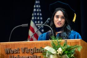 woman stands behind a podium in a graduation cap and gown