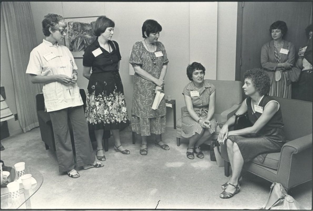 Black and white photo of women sitting in room, talking