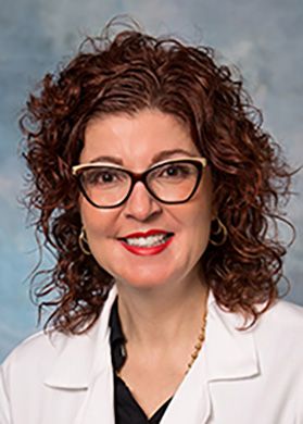 Headshot of Roberta Renzelli-Cain, associate professor at WVU. She is pictured against a light blue background wearing her white lab coat. She has curly red hair and wears black framed glasses. 