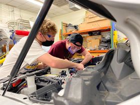 two people work under the hood of a vehicle 