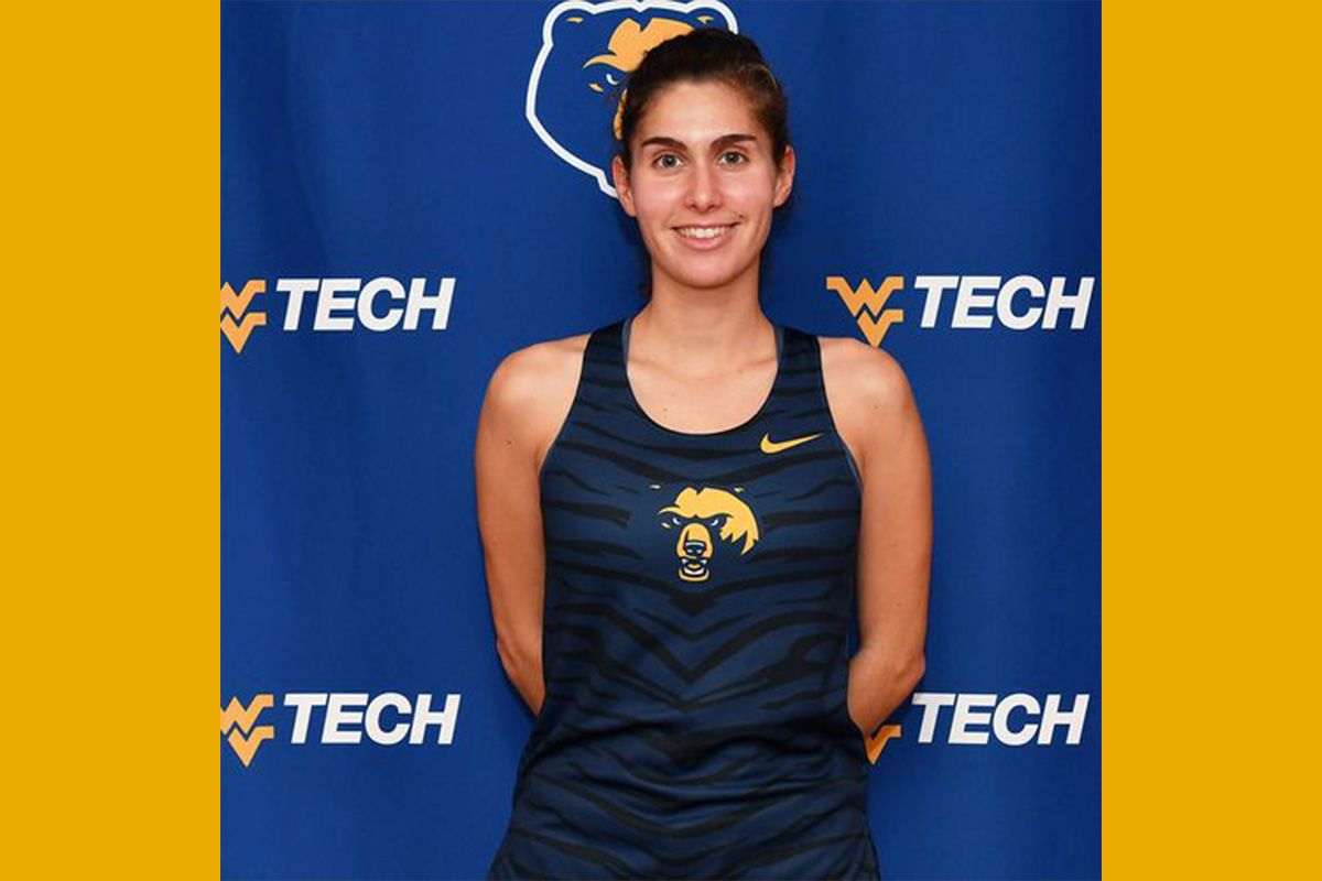 WVU Tech student Carmen Camino is shown here wearing her track uniform for an event. She has dark hair pulled back and is standing in front of a WVU Tech themed backdrop. 