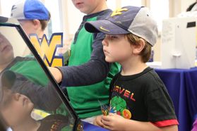 Young boy in a black t-shirt and wv hat plays a digital game while staring at a screen.