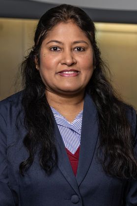 WVU professor Soumya Srivastava sits for a headshot wearing a navy blue jacket over a blue striped dress shirt. She has long dark hair pulled up from the sides. 