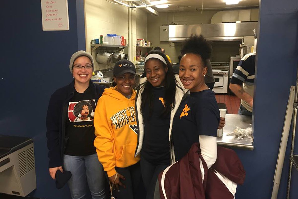 Four young women stand in a doorway; all are wearing WVU gear