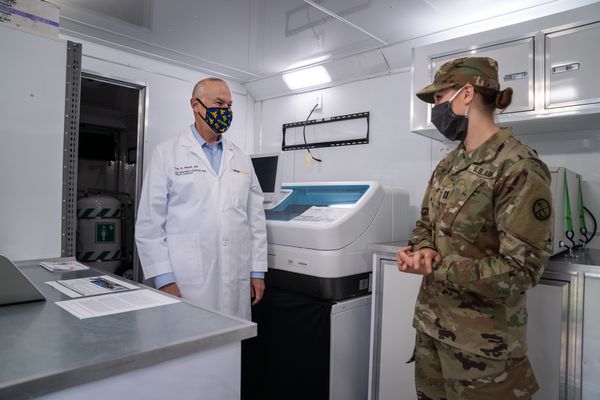 young woman in mask and military clothes in conversation with doctor in lab coat