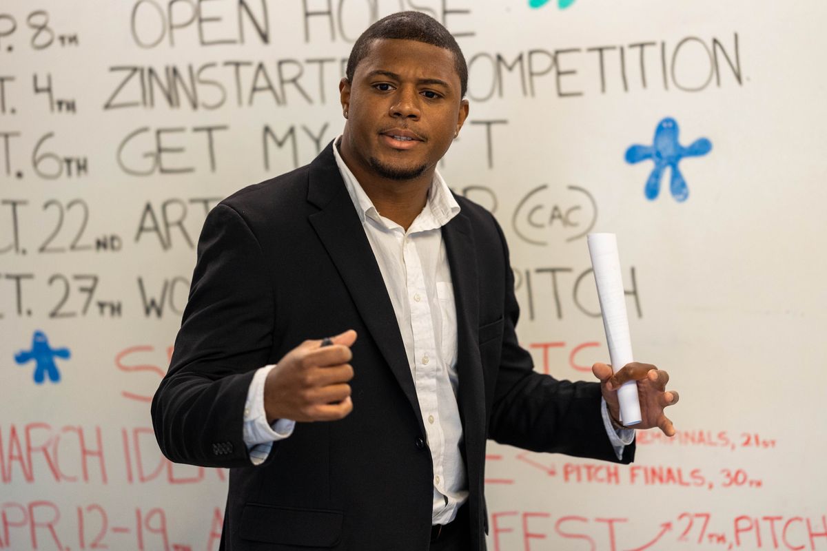 A person makes a presentation in front of a white board with the words 'Zinnstarter Competition' behind them.