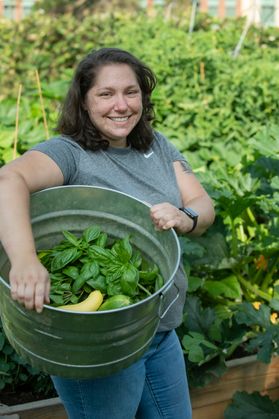 Woman standing in a garden holding a bucket of vegetables 
