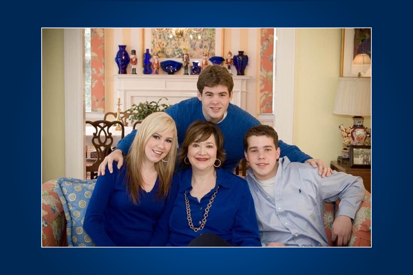 WVU donor pictured with her three children sitting on a couch in her living room. The donor is wearing a blue sweater, her daughter to the right has blonde hair and a blue sweater, and her to sons are to her left. 