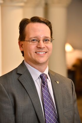 Headshot of WVU physics professor Paul Cassak. He is pictured inside of a building with soft lighting. He is wearing a gray suit with a light colored dress shirt and purple tie. He has short brown hair and is wearing eyeglasses. 