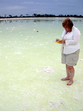 Benison stands in yellow body of water wearing white shirt and grey shorts writing on a yellow piece of paper