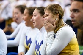 A member of the WVU Marching Band colorguard covers her face in excitement. Other band members are shown with smiles.
