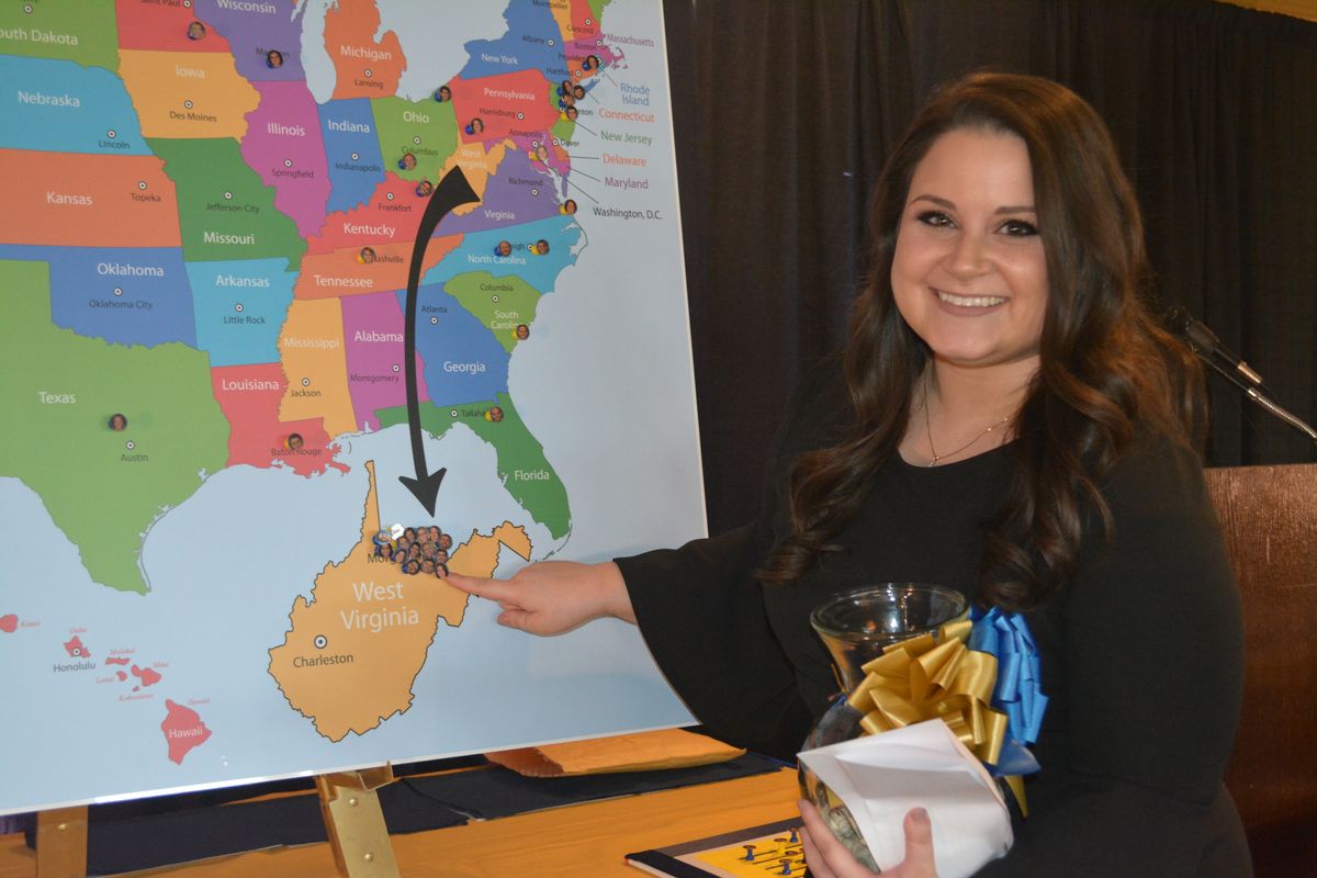 A young woman points to a map of West Virginia super-imposed outside a map of the U.S.