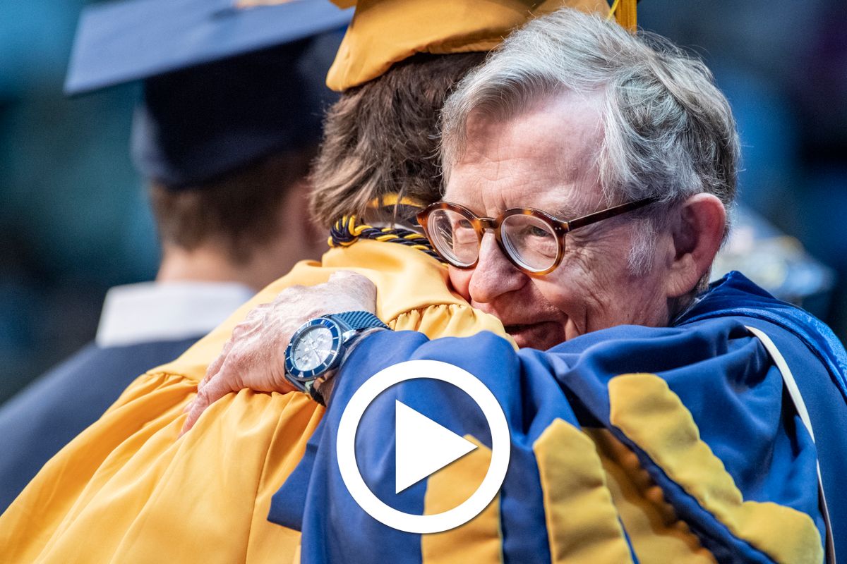 man hugs a college graduate as he receives his degree