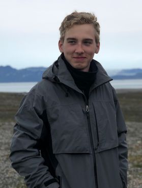 Photograph of WVU student Ian Bird. He is pictured standing outside with a scenic view behind him. He is wearing a winter coat and has light blonde hair. 