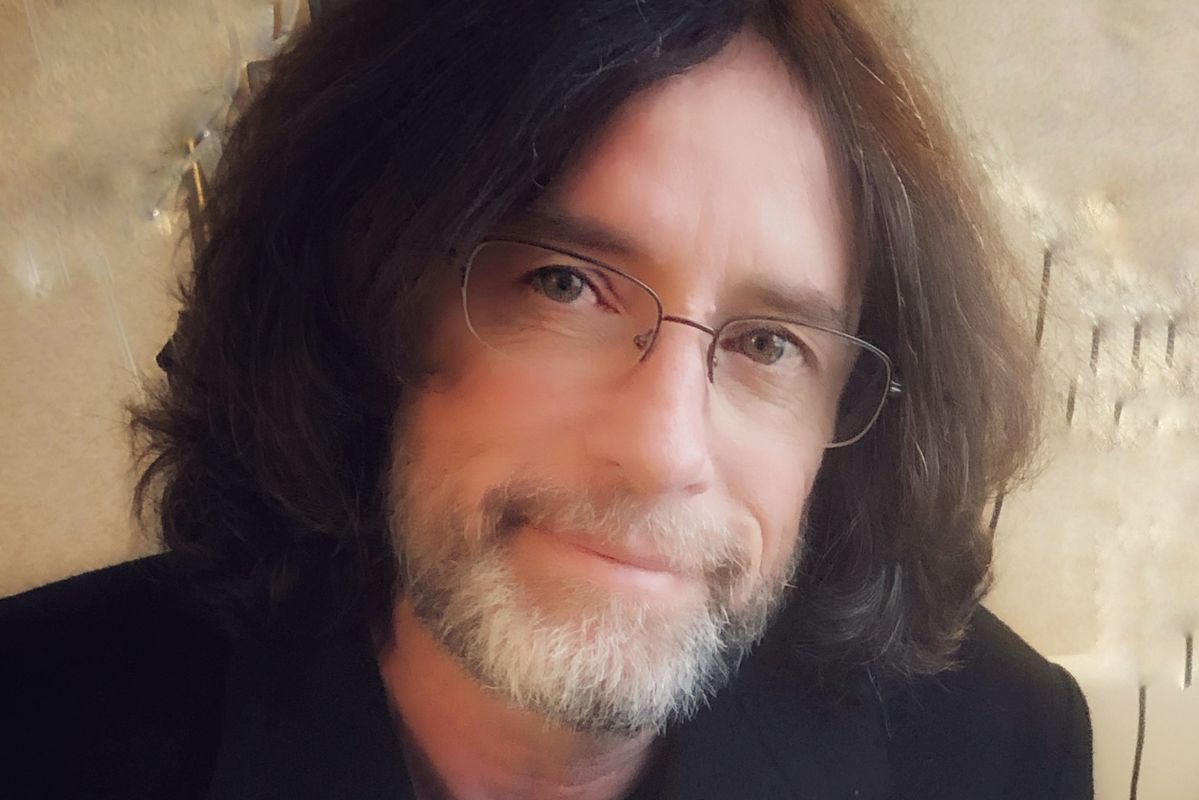 man with long brown hair and glasses smiles