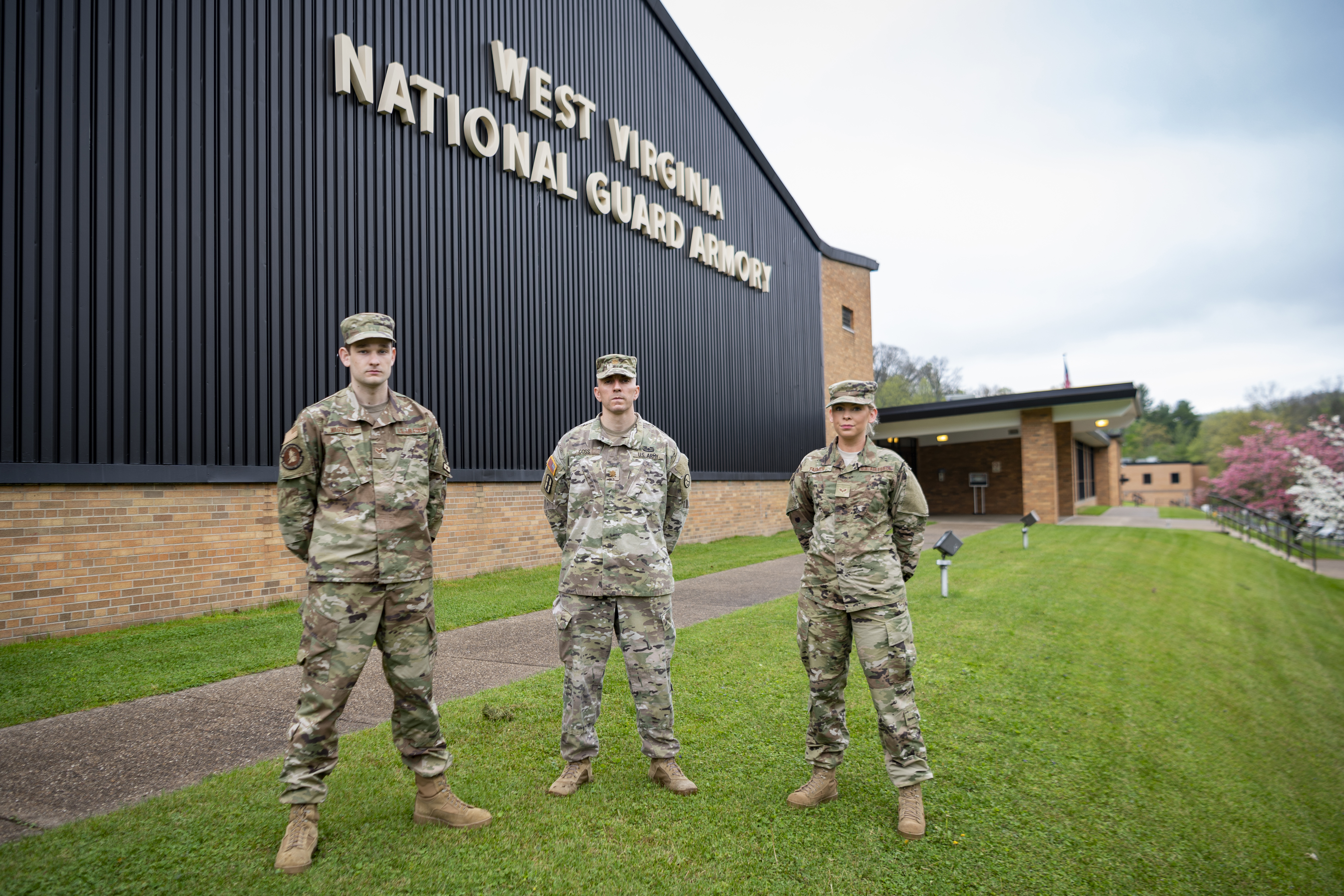 three men in camo uniforms stand in front of brick building