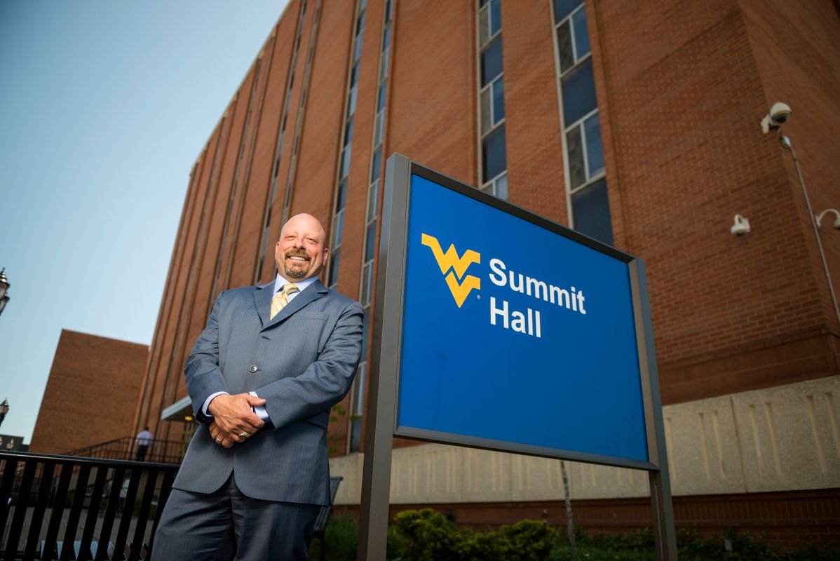 Bill Bayless stands beside WVU's Summit Hall sign