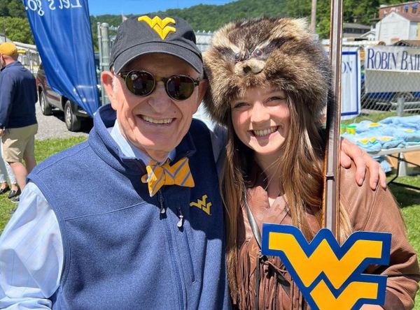 On the left, President Gee smiles at the camera while wearing a Flying WV hat, blue vest and gold bow tie. On the right is Mary Roush, the Mountaineer Mascot