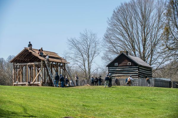 Photo of workers working on two barns surrounded by grass and trees. 